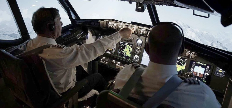 Pilots navigating airplane cockpit during flight with mountain view in background