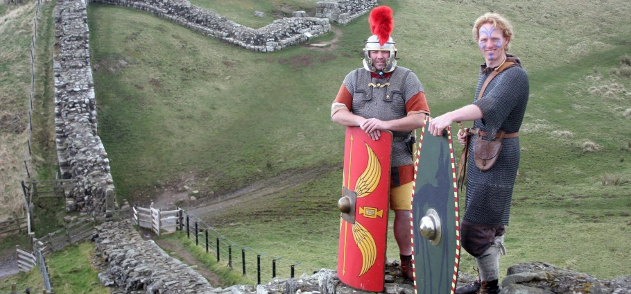 Two men in Roman soldier costumes standing on Hadrian's Wall in England, holding shields and wearing traditional armor.