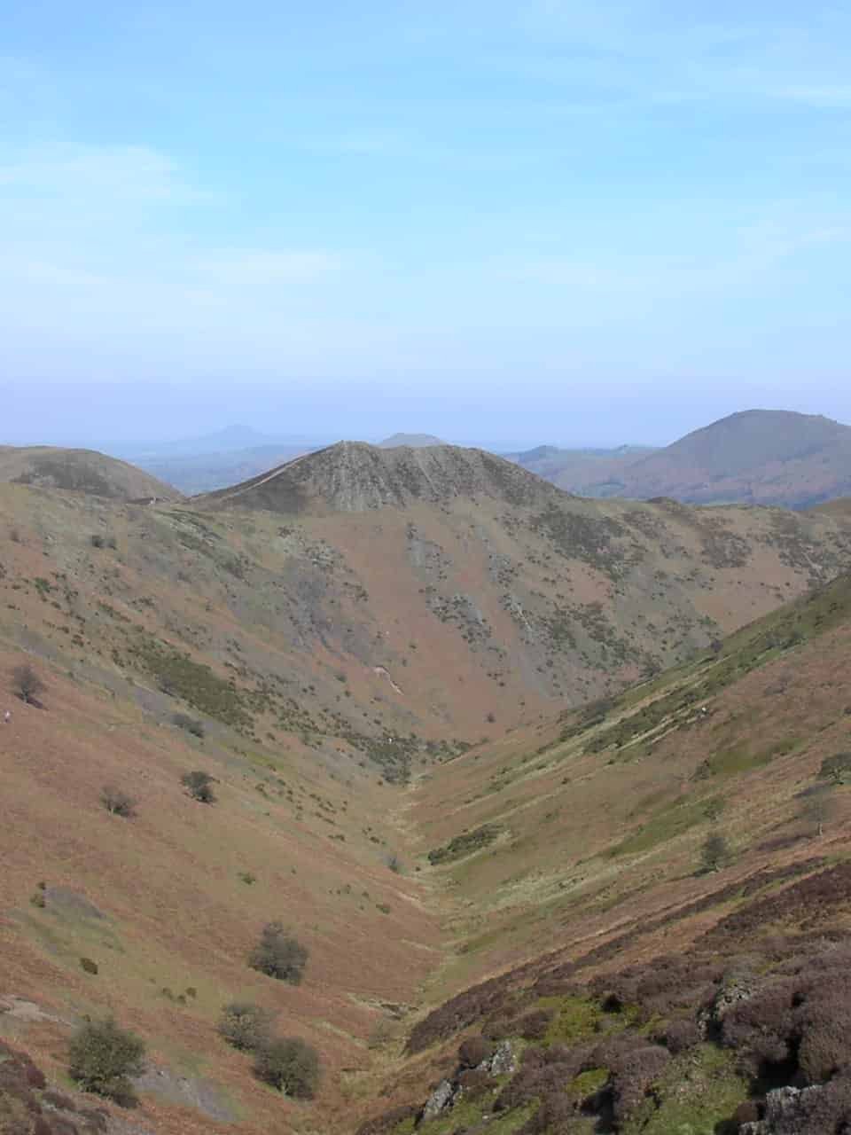 Scenic view looking down a deep, steep-sided valley in the Shropshire Hills, with rolling brown and green hills extending toward the horizon.