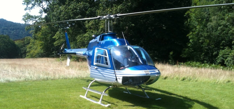 Blue and white helicopter parked on grassy field with trees in the background.