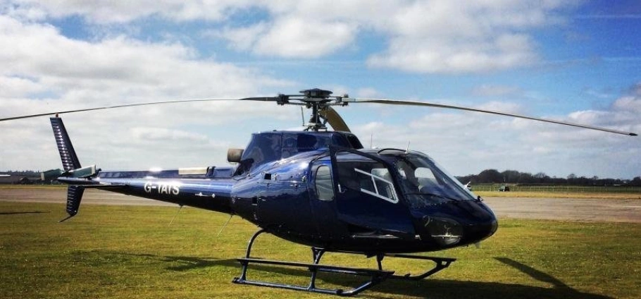 Blue helicopter parked on grassy field under cloudy sky.