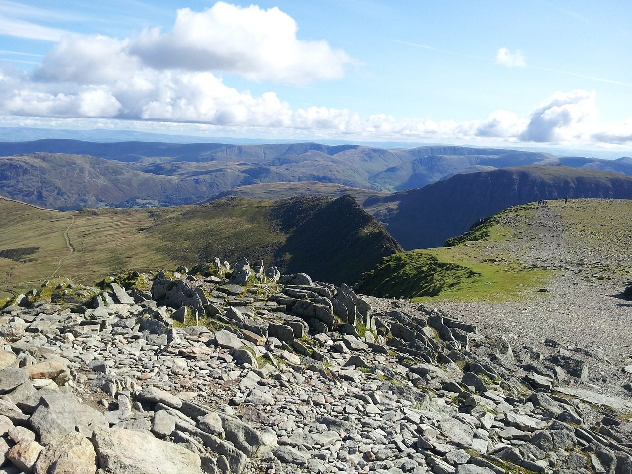 Panoramic view from a mountain summit, showcasing rocky terrain, rolling hills, and distant valleys under a blue sky with scattered clouds. Ideal for nature enthusiasts and hikers exploring scenic landscapes.