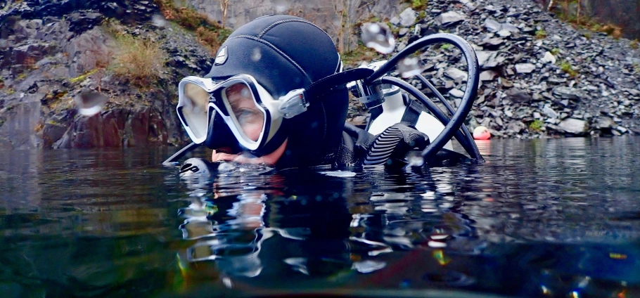 Scuba diver in wetsuit and mask swimming in a rocky water area