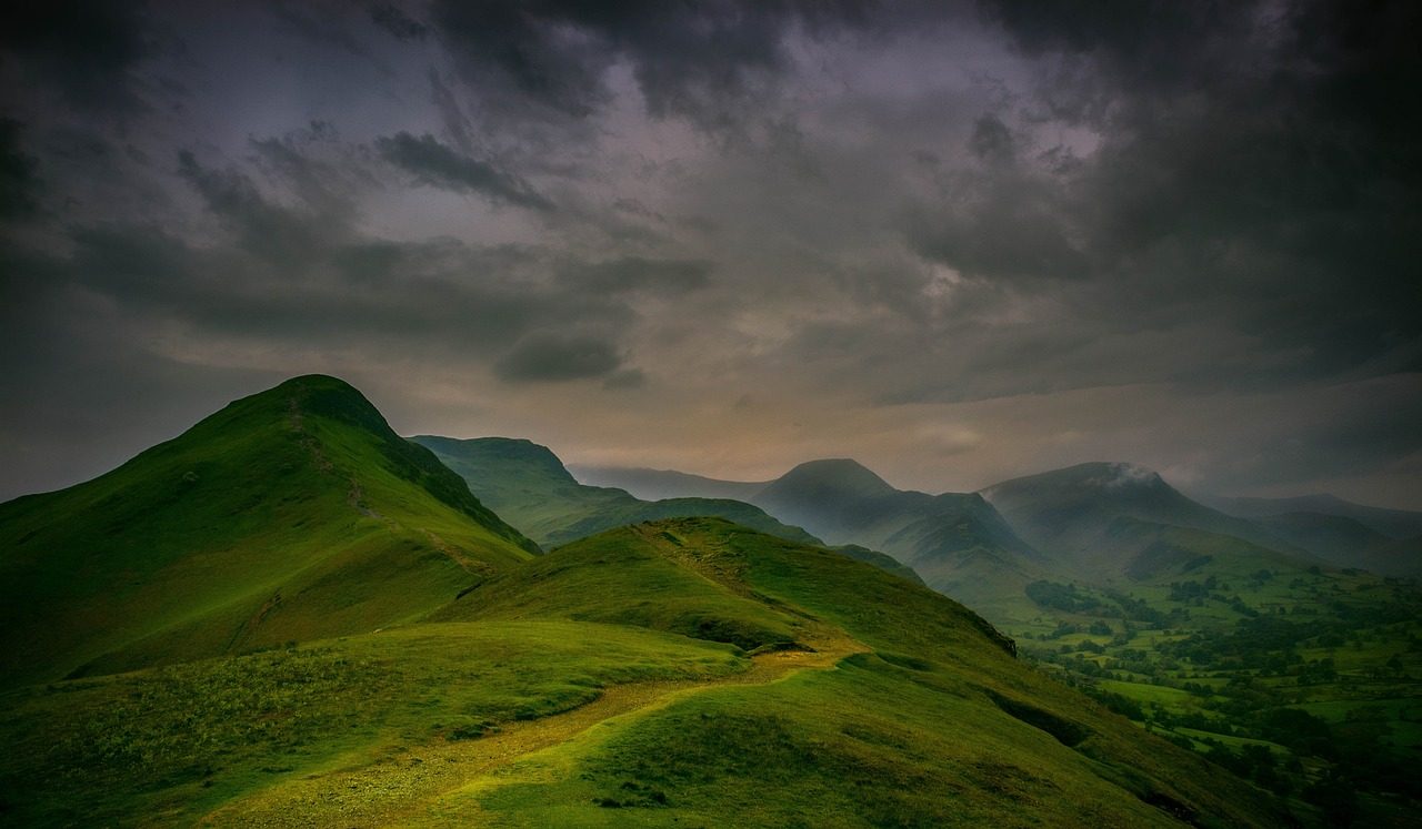 Lush green hills under a dramatic cloudy sky, showcasing a scenic landscape with rolling mountains and valleys, ideal for outdoor enthusiasts and nature lovers.