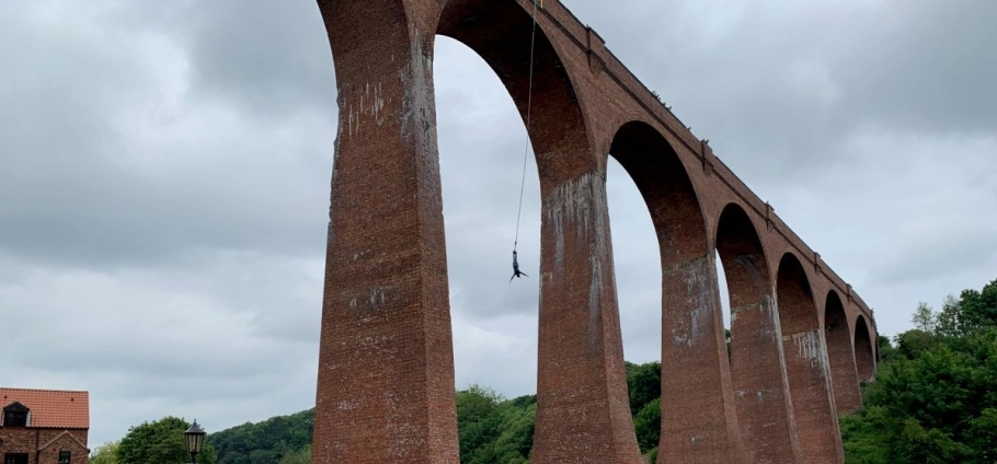 Person bungee jumping from a tall brick arch bridge on a cloudy day