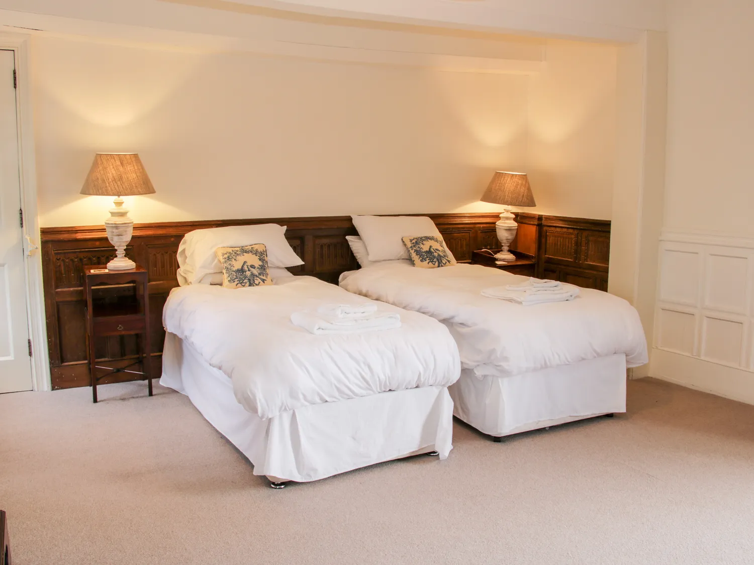 Cozy twin bedroom with white bedding, wooden headboards, bedside tables, and warm lighting from table lamps.