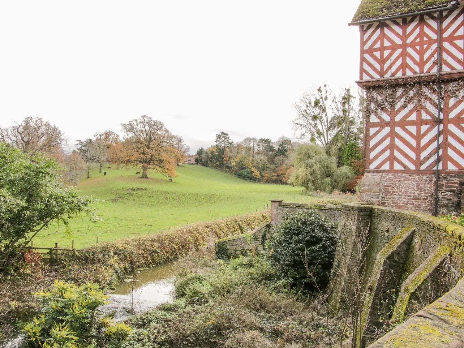 Historic half-timbered building with scenic countryside view, lush green fields, and autumn trees in the background.