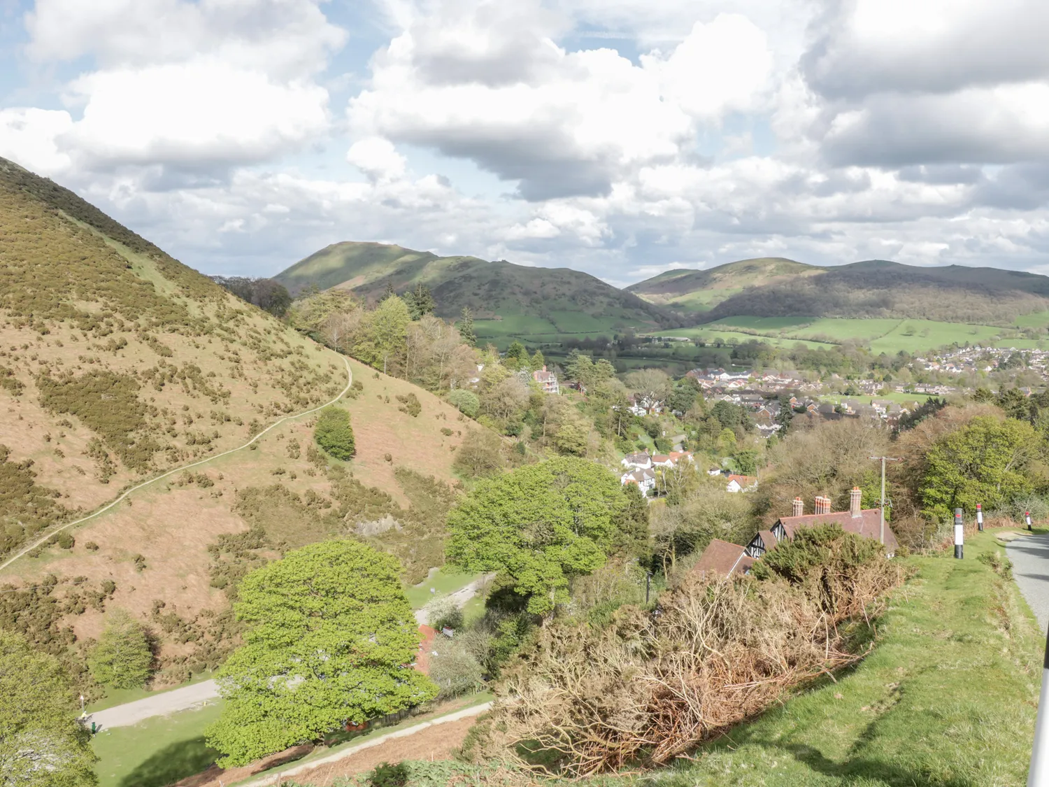 Scenic view of rolling green hills and a small village nestled in a valley under a partly cloudy sky.