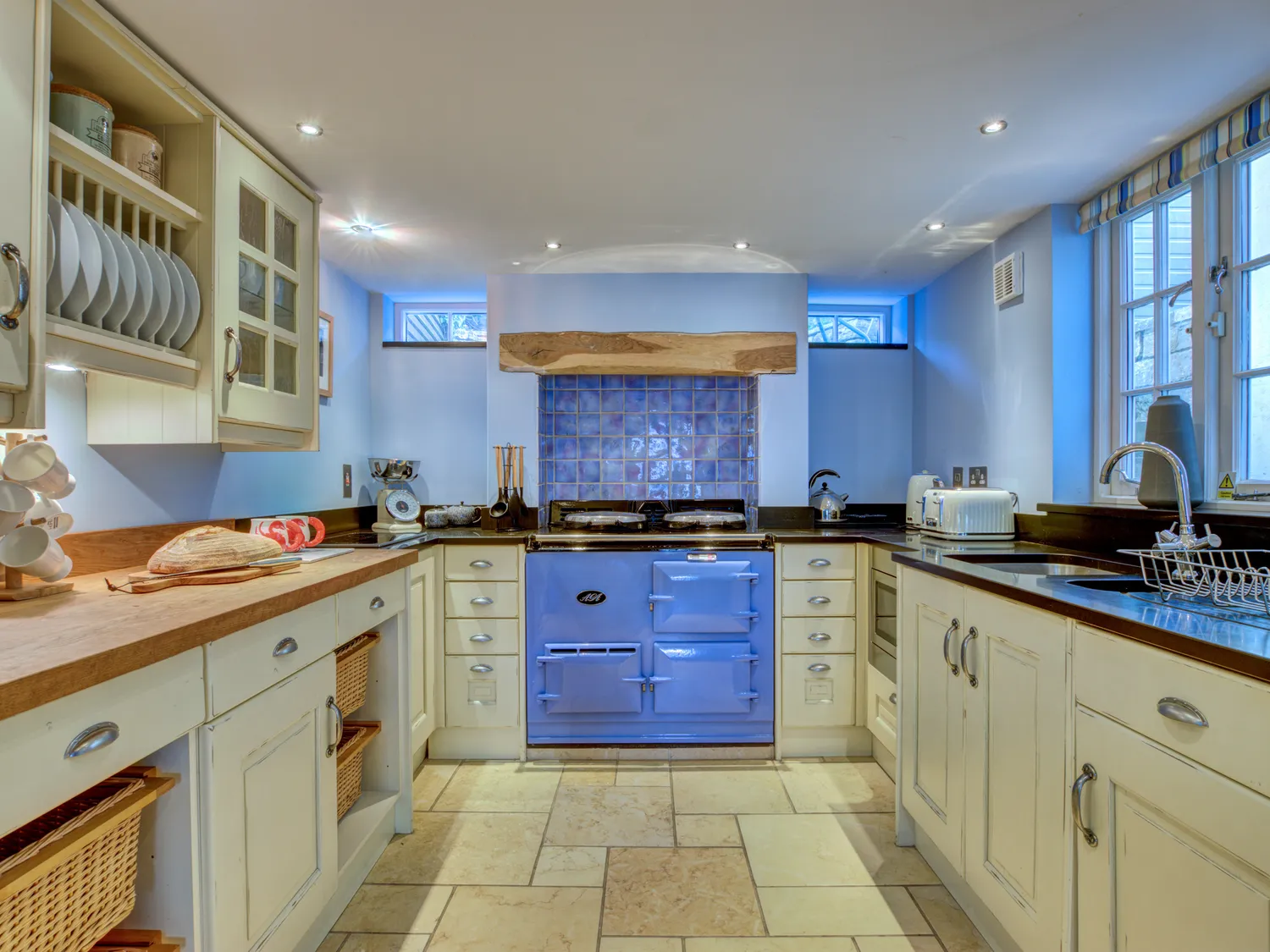 Crab Cottage, Modern farmhouse kitchen with light blue walls, white cabinets, wooden countertops, and a blue vintage stove.