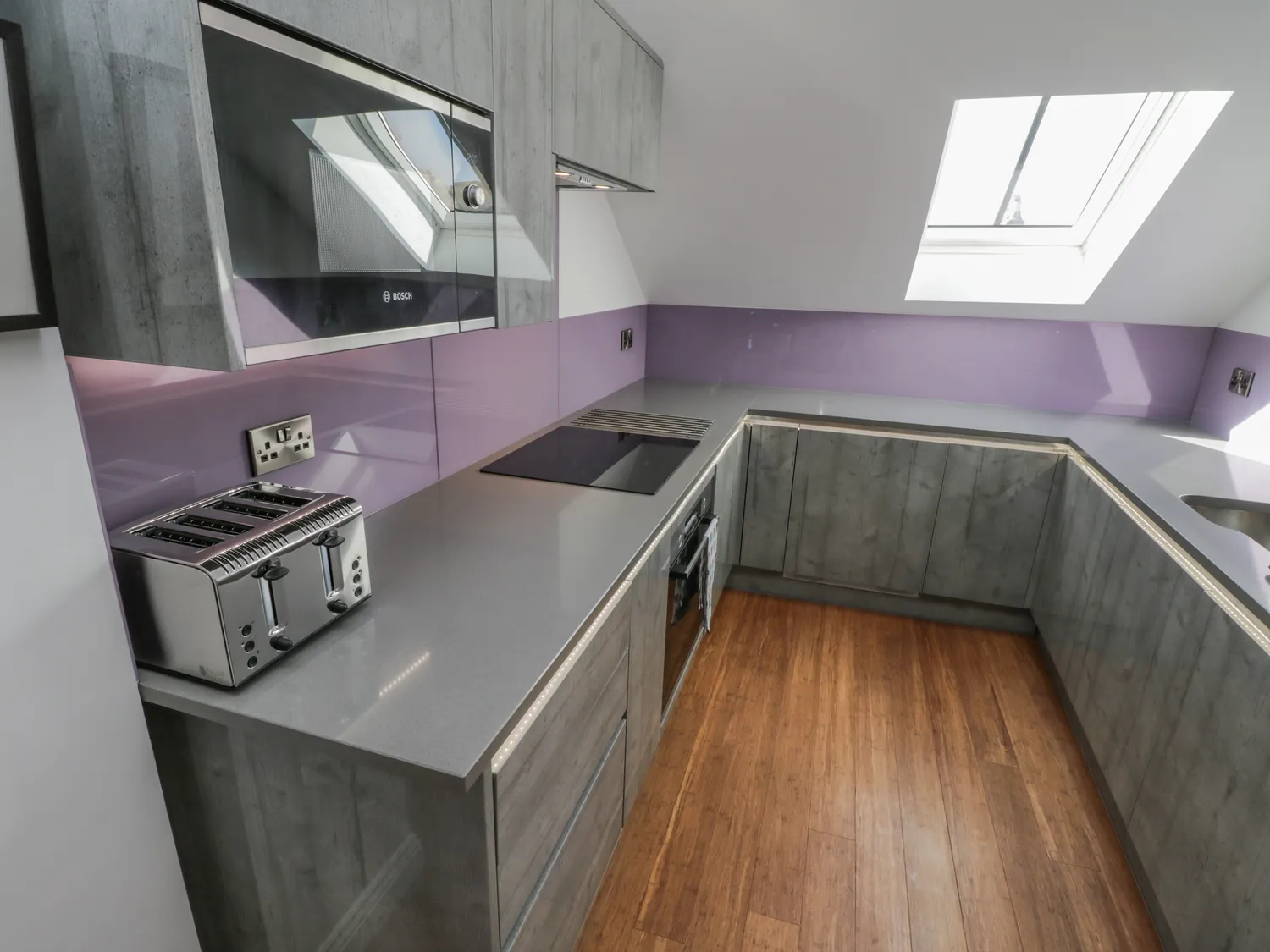 Modern kitchen design featuring gray cabinetry, sleek countertops, and a stainless steel toaster, with a purple backsplash and skylight for natural light.