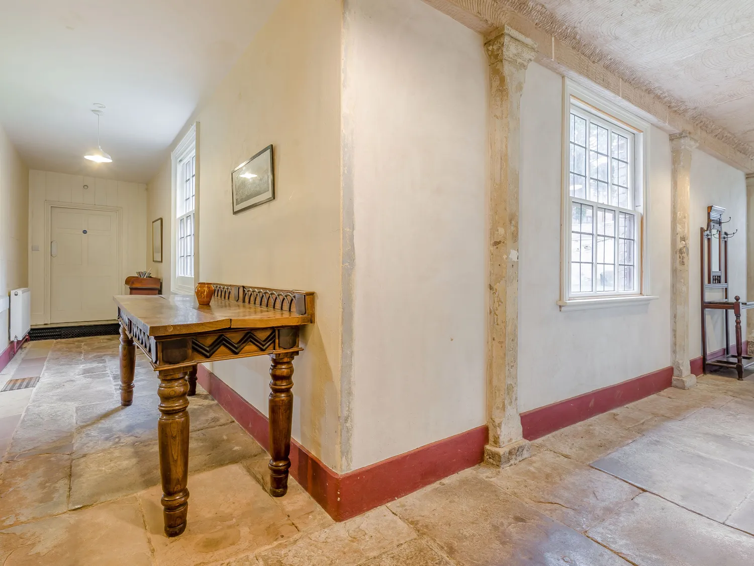 Historic hallway with stone flooring, wooden table, and large windows providing natural light.