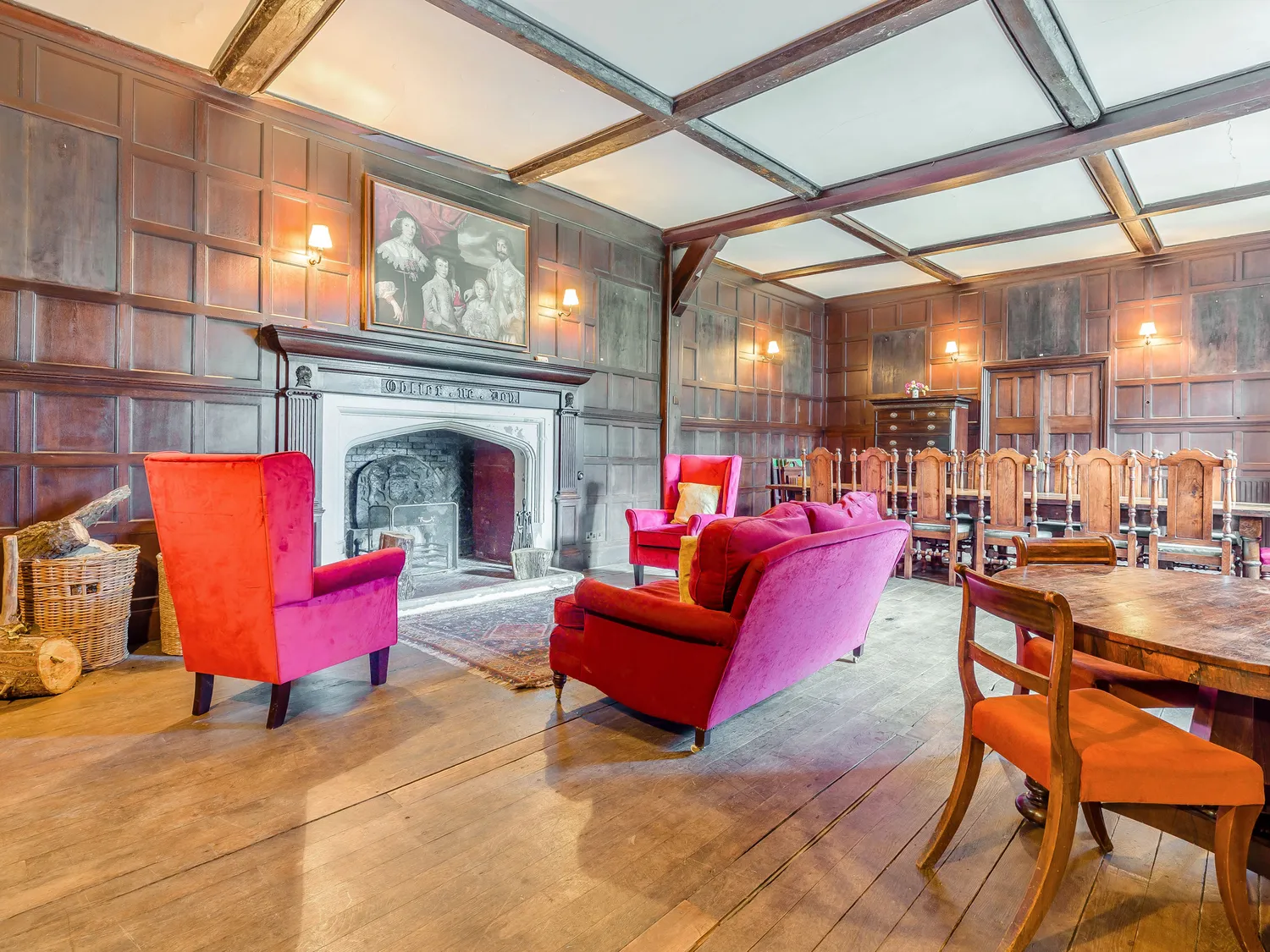 Historic room with wooden paneling, red velvet chairs, a large fireplace, and a long dining table with chairs.