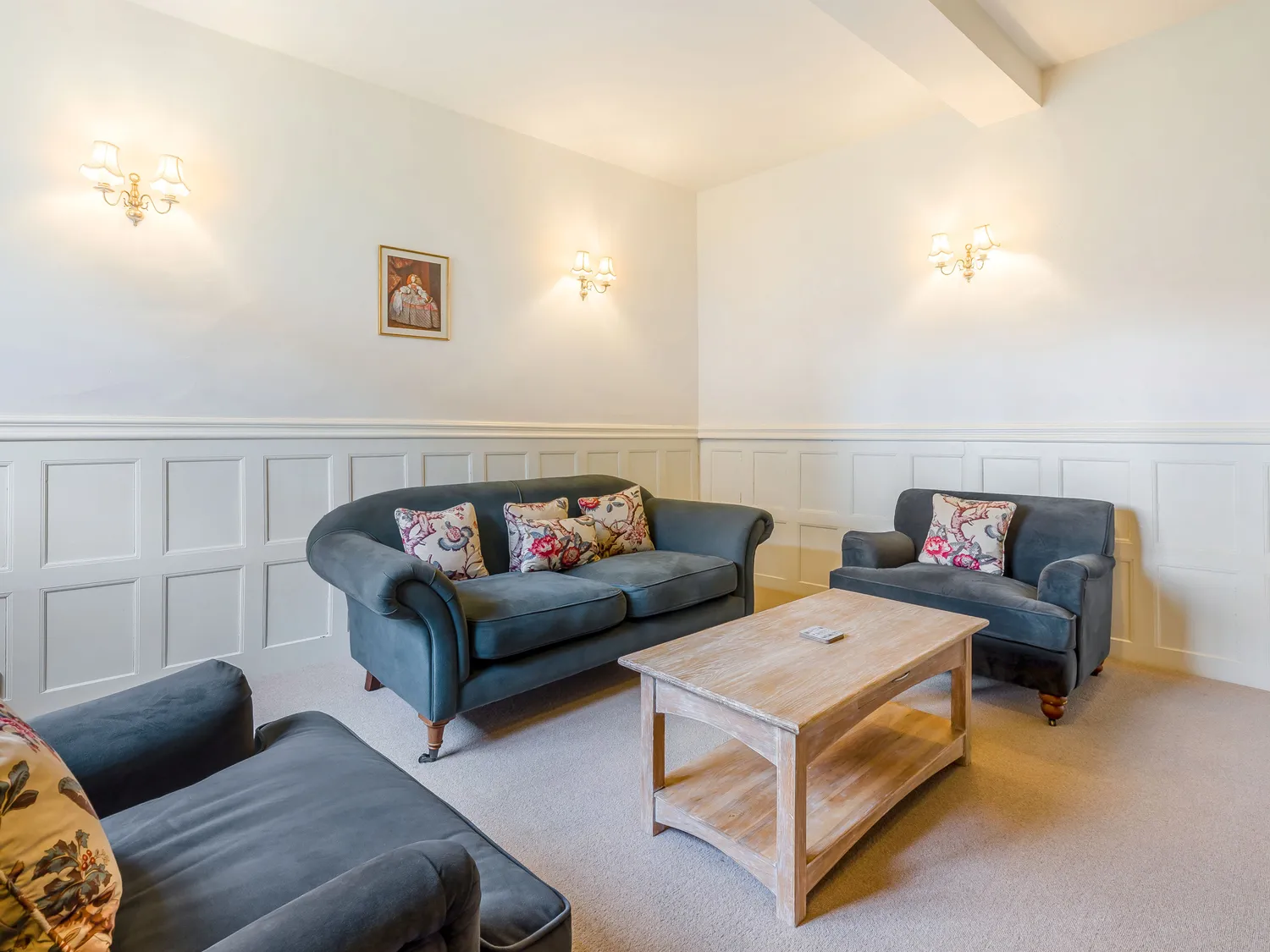 Cozy living room with blue sofas, floral cushions, wooden coffee table, and wall sconces.