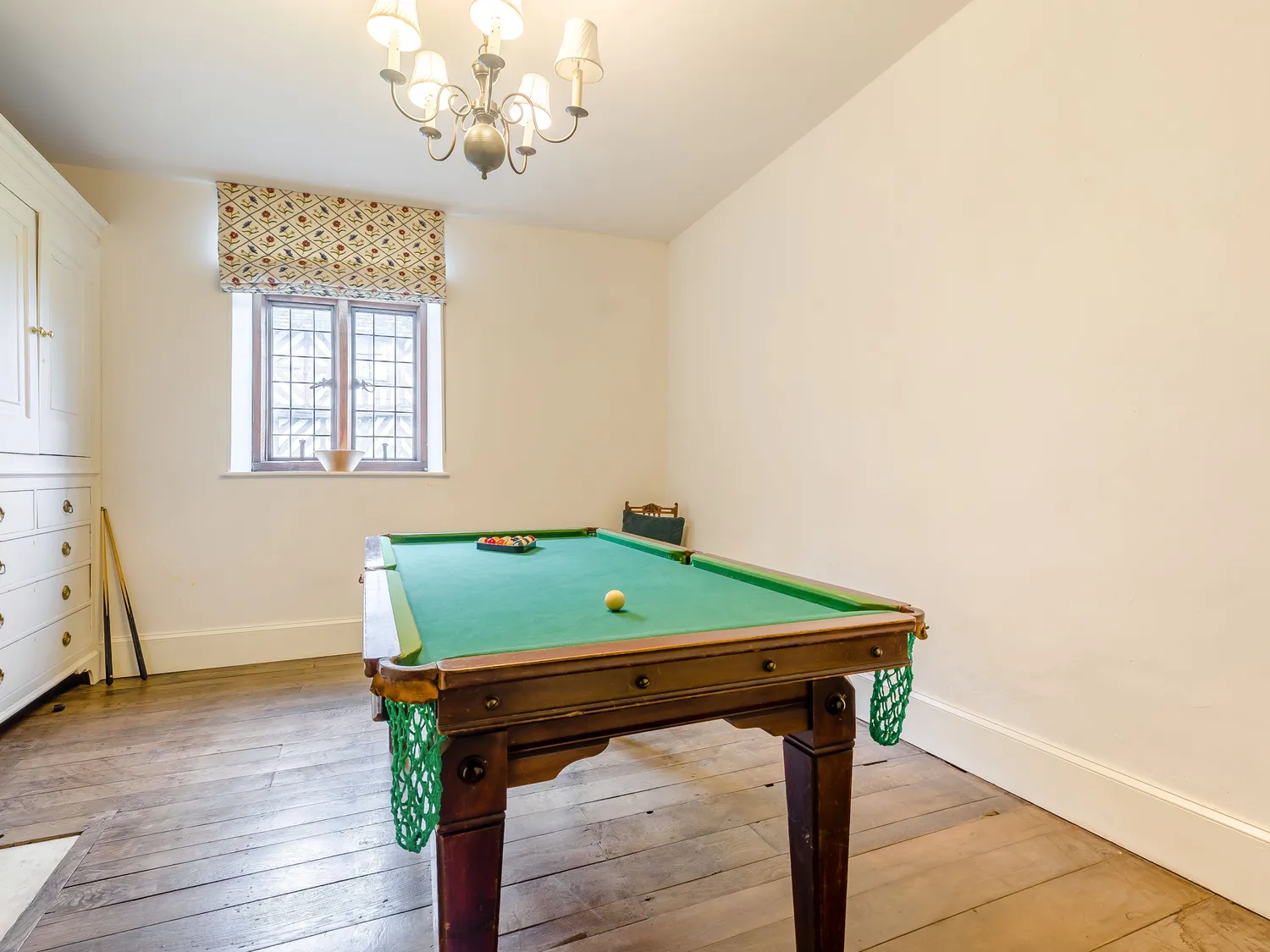 Small game room with a pool table, wooden floor, and a window with patterned curtains.