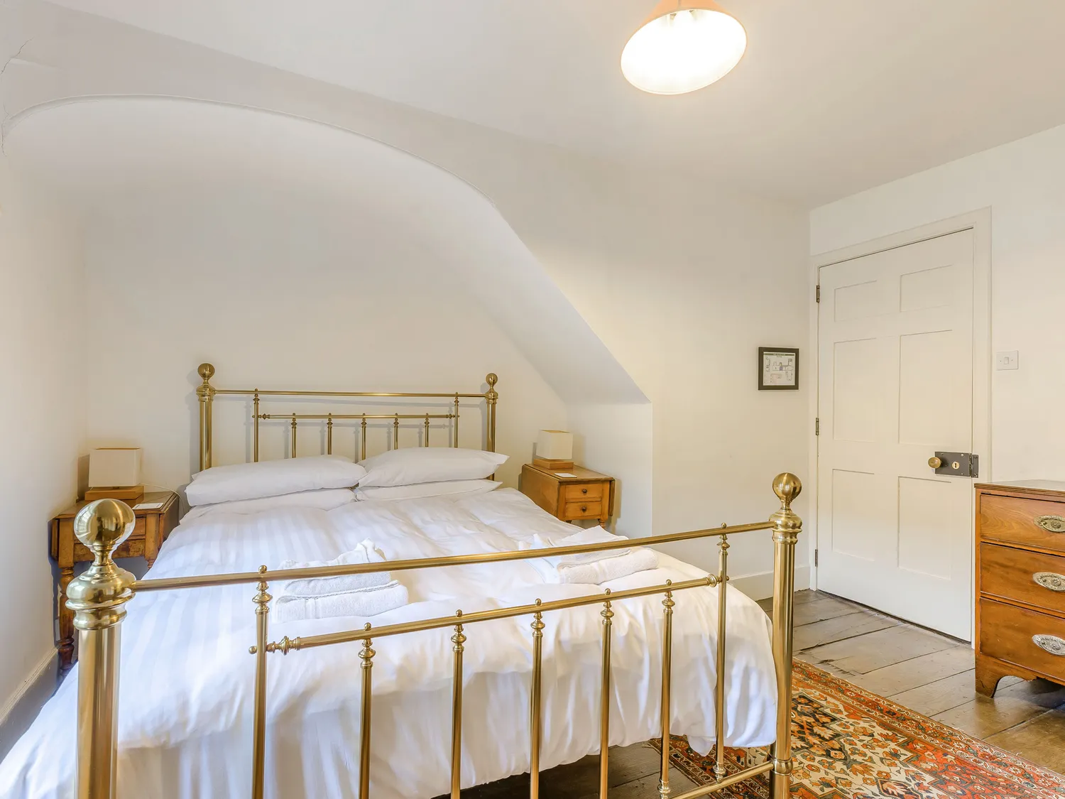 Cozy bedroom with brass bed frame, white bedding, wooden nightstands, and vintage decor.