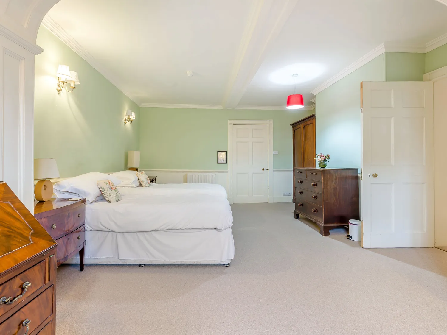 Spacious bedroom with light green walls, double bed, wooden dressers, and soft lighting.