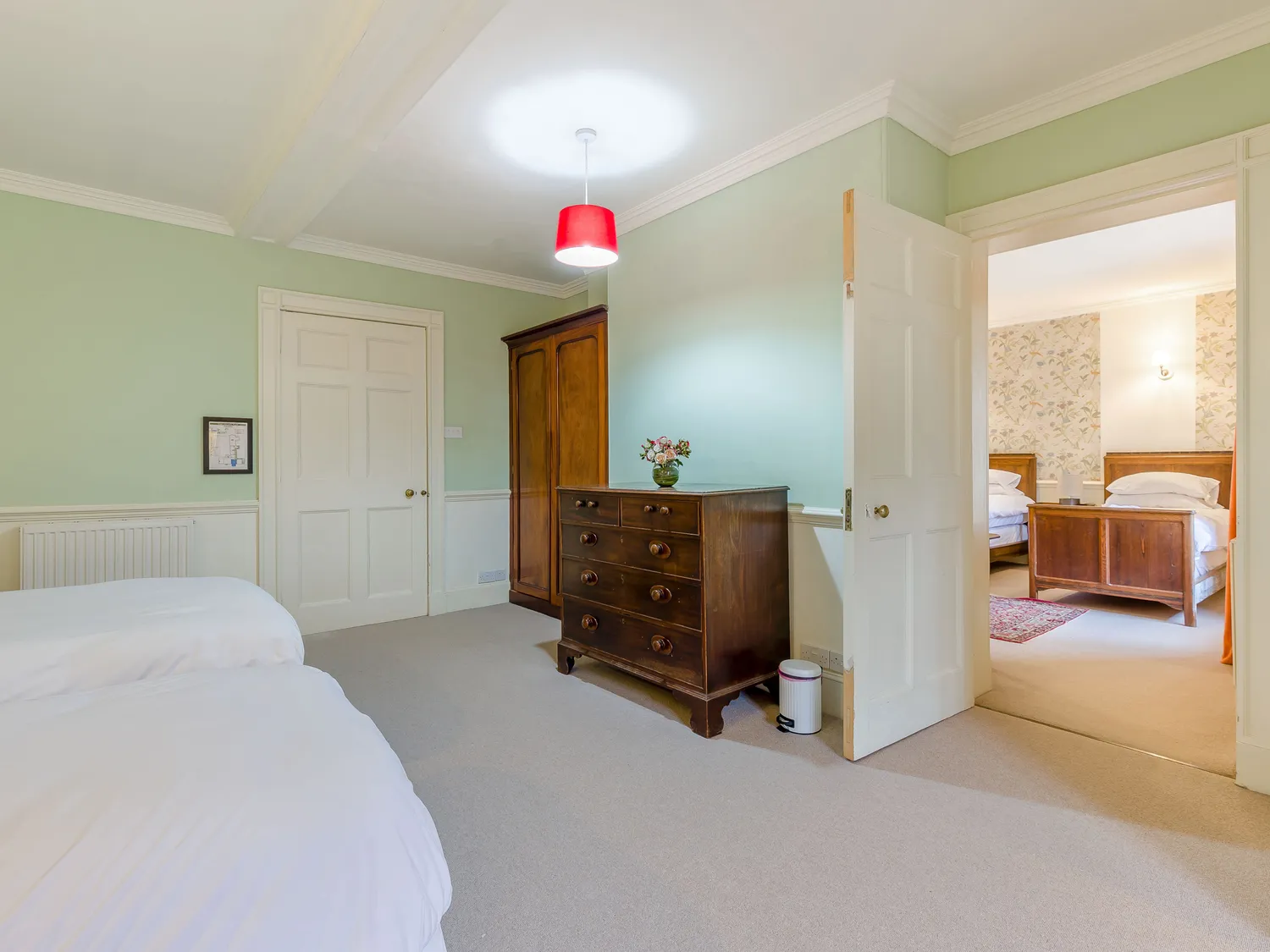 Spacious bedroom with twin beds, vintage wooden furniture, green walls, and an adjoining room with additional beds.