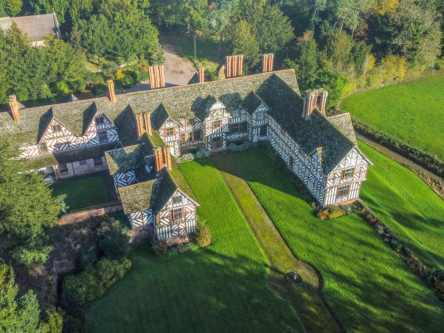 Aerial view of a historic Tudor-style mansion surrounded by lush greenery and gardens.