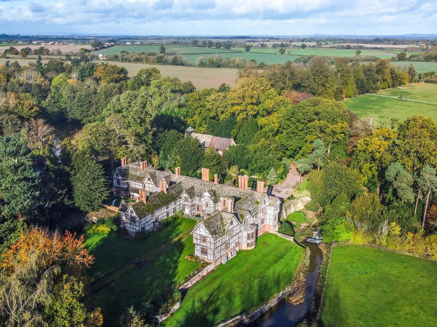 Aerial view of a historic mansion surrounded by lush greenery and expansive fields.