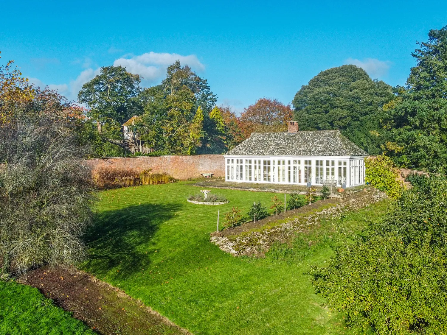 Charming countryside house with large windows surrounded by lush green garden and trees under a clear blue sky