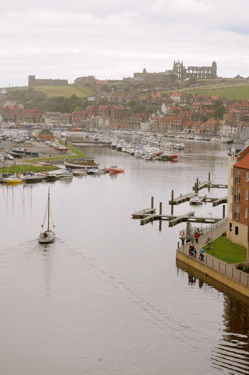 Scenic view of Whitby Harbour with boats docked, historic Whitby Abbey ruins on the hill, and waterfront buildings in Whitby, England.